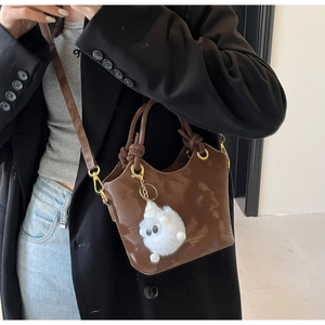 Detail einer glänzenden braunen Beuteltasche mit Plüschschaf-Anhänger und Schulterriemen