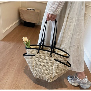 Detail of a large woven straw tote bag with black trim and a yellow tulip accent