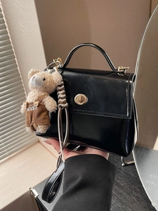 Elegante bolso de hombro negro con un lindo amuleto de oso y cierre giratorio dorado
