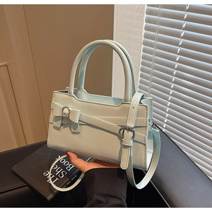 Detail of mint green handbag with bow decoration and silver buckle in a hand-held view