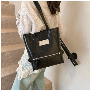 Détail du sac cabas en cuir noir brillant avec plaque métallique et poche zippée décorative