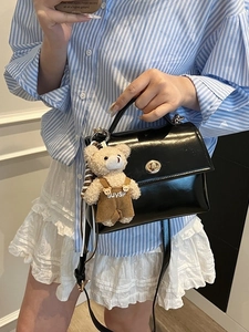 Bolso de hombro de charol negro con colgante de osito y cierre de giro metálico elegante