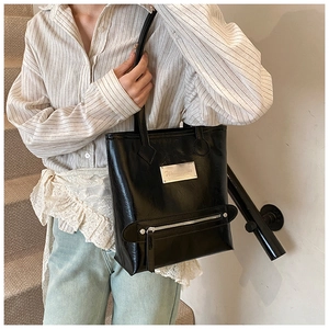 Detail of black glossy tote bag with silver metal plaque and decorative zipper