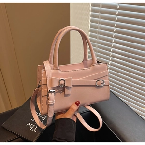Detail view of pink square handbag with bow and silver buckle held in hand