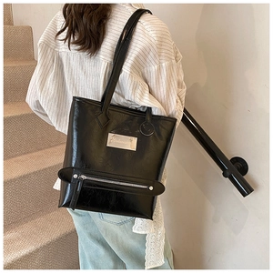 Détail du sac cabas noir brillant avec plaque logo argentée et texture plissée