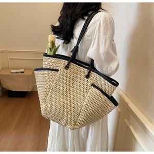 Detail view of large straw tote bag with black leather straps on a female model