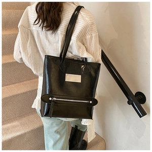 Close-up of black glossy tote bag featuring silver metal logo plate and zipper details