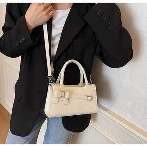 Close-up of beige leather handbag with bow detail on a model in a black suit