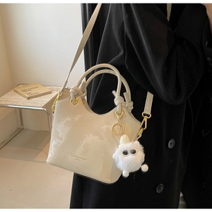 Detail der cremefarbenen Eimertasche mit Knotengriff und Plüschtier auf schwarzem Outfit
