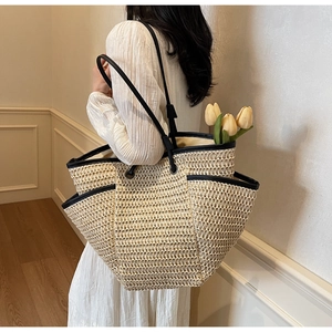 Detail of a beige straw tote bag with black leather trim and spacious side pockets