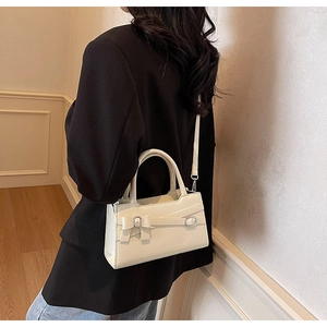 Detail of cream white leather handbag with buckle accent worn with a black blazer