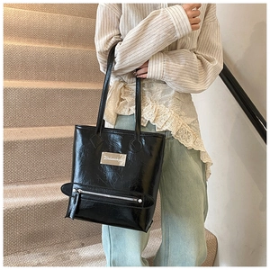 Détail du sac cabas en cuir verni noir avec poche zippée et plaque métallique logotée
