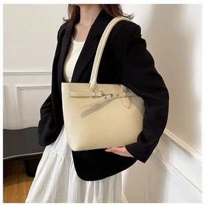 Détail du sac fourre-tout crème avec texture litchi et boucle sur l'épaule du mannequin