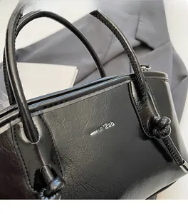 Dettaglio borsa tote nera in pelle lucida con logo argento e manico con nodo unico