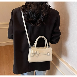 Close-up of cream handbag with decorative bow and silver buckle worn on black blazer