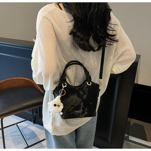 Detail der schwarzen glänzenden Leder-Eimertasche mit weißem Fellanhänger und Gurt