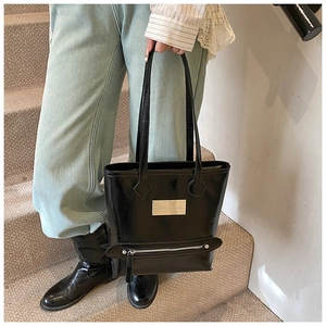 Detail of glossy black tote bag featuring a silver logo plate and decorative zipper