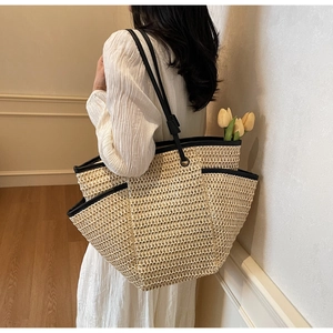 Detail of a large woven straw tote bag featuring contrast black trim and shoulder straps
