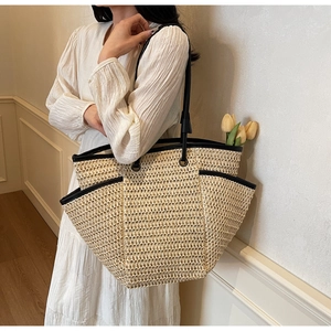 Detail of hand-woven straw tote bag with black leather straps and front pocket detail