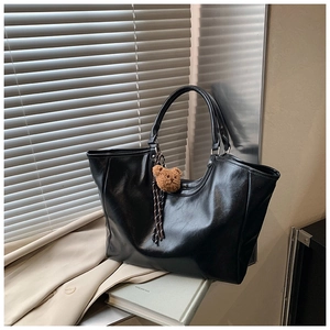 Detail of black faux leather tote bag featuring a brown plush bear charm on window ledge