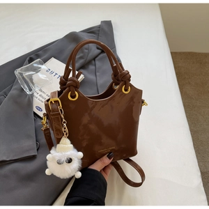Detail einer braunen Lackleder-Beuteltasche mit Goldschrift und Plüsch-Schafanhänger