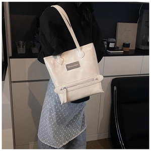 Close-up of ivory tote bag featuring glossy wrinkled leather and silver brand plaque