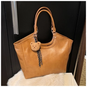 Detail of caramel lychee grain leather tote bag with plush bear charm on white fur rug
