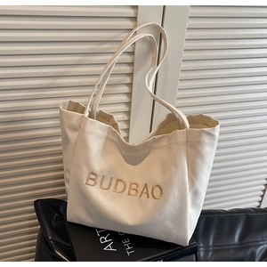 Detail of off-white canvas tote bag featuring brown letter print and reinforced straps