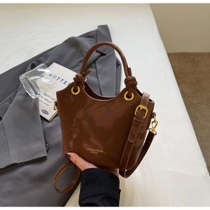 Detail einer braunen matten Kunstleder-Beuteltasche mit Gold-Hardware auf grauem Blazer