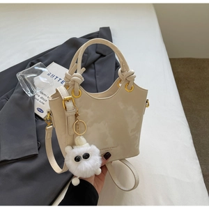 Detail der beigen Beuteltasche mit geknotetem Griff und flauschigem Monster-Anhänger