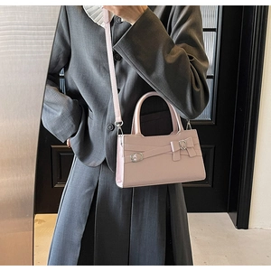Detailed view of light pink handbag with bow design held by a model in a grey suit