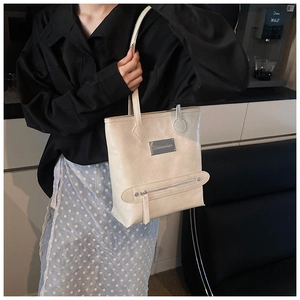 Detail shot of a large beige leather tote bag with a metal logo and front zipper pocket