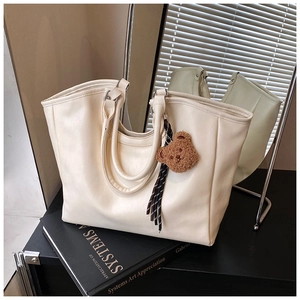 Detail of cream tote bag with plush bear charm and striped ribbon in modern setting