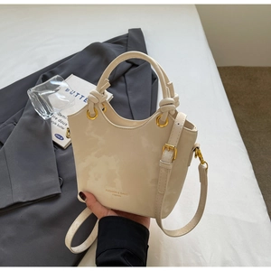 Detail der cremeweißen Beuteltasche mit dekorativem Knotengriff und goldenen Beschlägen