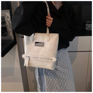 Detailed macro view of the cream white tote bag featuring the silver metal brand logo plate