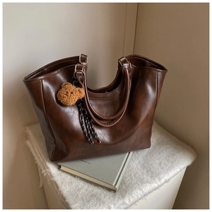 Detailed shot of brown leather tote bag featuring a cute teddy bear charm and braided strap