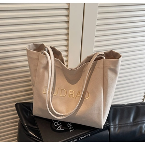 Close-up of beige canvas tote bag featuring yellow BUDBAO embroidery and wide straps