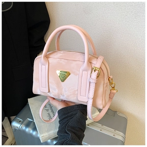 Détail du sac bowling rose avec texture marbrée et plaque dorée sur une valise argentée