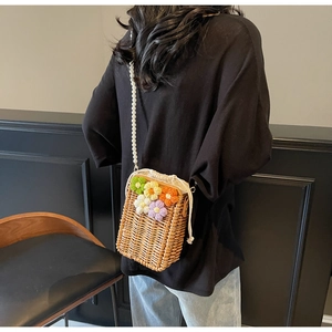 Détail d'un sac seau en paille tressée avec fleurs au crochet et bandoulière en perles