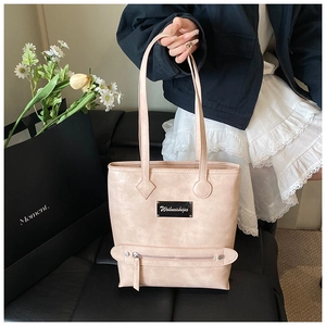 Detail of a large pale pink tote bag featuring a black metal logo and front zipper pocket