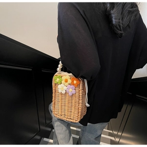 Détail d'un sac seau en paille avec fleurs au crochet et anse en perles blanches