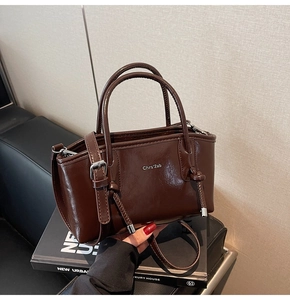 Dettaglio di una borsa tote in pelle marrone scuro lucida con manici ad anello e tracolla