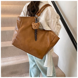 Detail of caramel leather tote bag with plush bear charm and striped ribbon on shoulder strap