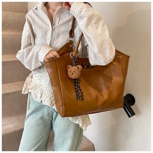 Detailed texture of brown PU leather tote bag with a cute plush bear charm accessory