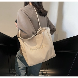 Detail of beige canvas tote bag featuring yellow BUDBAO embroidery and long shoulder straps