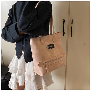 Model showing apricot faux leather tote bag with metal nameplate and zipper detail