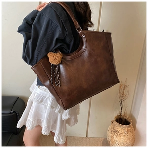 Brown faux leather tote bag with stylish teddy bear charm and wide shoulder strap