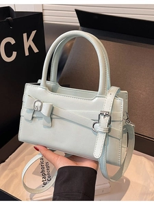 Chic light green handbag with bow detail and adjustable shoulder strap shown in hand