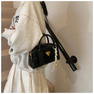Détail du sac bowling noir avec logo triangle doré et charms en foulard de soie géométrique