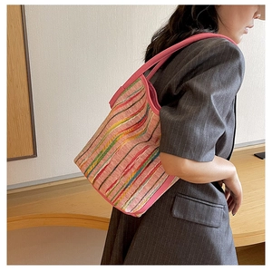Close-up of a pink woven bucket bag with colorful stripes and leather trim on a model
